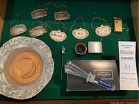 Overview of crystal stopper, metal label tags, glass plate, lighter, cocktail pick, cigarette case, and bottle opener/coaster.