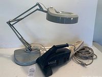Complete view of gray adjustable work lamp with magnifying glass and black Little Lux handheld vacuum with attached cords.