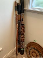 Two Aboriginal digeridoos, wooden walking stick with badges, and woven basket partially visible on the floor.