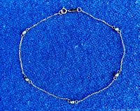 Full view of thin gold bracelet laid flat on blue background showing six grey beads spaced along a delicate gold chain with a round spring clasp closure.
