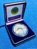 Photo of Kazakhstan silver coin in original clamshell case showing coin in protective plastic capsule and Certificate of Quality with Kazakh national emblem.