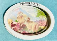 Top view showing the oval porcelain baby feeding bowl with detailed painted scene of lambs and labeled 'BABY'S PLATE' on rim.