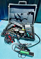 Car tune-up kit inside black carrying case showing remote starter, tool with dials, cables, and tester device.