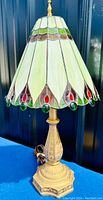 Front angled view of the leaded stained glass table lamp showing the conical shaped shade with multi-colored glass panels and ornate decorative metal base.