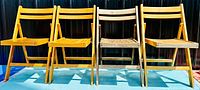 Four vintage mid-century modern wooden folding chairs in a row against a black background showing front view and all folded for storage.