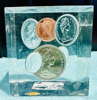Front view of clear Lucite cube showing 5 Canadian coins including the copper penny and silver-colored coins with Queen Elizabeth II portrait.