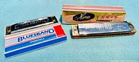 Two vintage harmonicas with their original boxes, one Bluesband by Hohner International in a blue, white, and red box and one Alexo harmonica in a gold and pink box with Chinese characters.