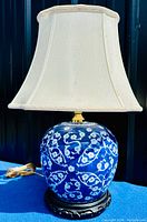 Full view of the lamp showing blue and white ginger jar base, white fabric lampshade, and power cord on blue surface