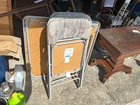 Card table and four folding chairs stacked and folded showing seats and backs of chairs with patterned fabric and bottom of table with folding legs.