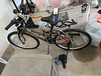 Oblique overview of the CCM Cabrera mountain-style bike highlighting frame, wheels, and included extra seat and lock on the floor.