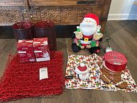 Photo showing the Christmas items including red placemats, red candle holders, Santa Claus figurine, gingerbread pot holder and ribbon spool.
