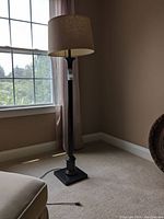 Full view of tall metal floor lamp with linen-look cylindrical shade near window.
