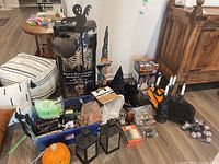 Assortment of Halloween decorations on a hardwood floor including lanterns, spiderweb mats, skeleton and witch figures, and other decor.