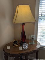 Jean Roulet table clock, glass base red lamp with beige shade, Orrefors candle holder, modern clear glass clock on small wooden table.