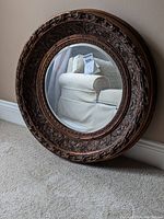 Photo of entire round mirror showing carved wood frame and beveled edge glass reflecting a couch.