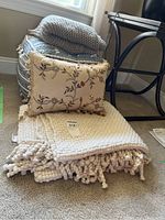 Woven cube ottoman topped with folded throw and floral pillow in front on carpet.