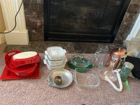 Overview of entire lot on carpet in front of fireplace showing all items grouped including bakeware, serveware, glassware and kitchen accessories.