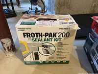 Sealed cardboard box of Froth-Pak 200 spray foam sealant kit on concrete floor.