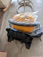 Wall mounted bright yellow Hawkeye shop vacuum cleaner unit wrapped in plastic, with black flexible hose and black mounting bracket.