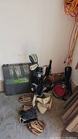 Baseball gloves on floor with golf bag and tennis racquets in corner, grey mats and baseball bag nearby