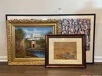 Three framed artworks leaning against a wall: largest is a Jackson Pollock mural poster, middle is a gold-framed oil painting of a landscape with white buildings, smallest is a framed sketch of boats signed Ramon.