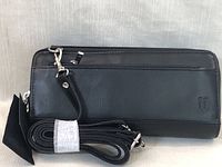 Black leather wallet exterior with detachable shoulder strap coiled beside it, showing zipper and subtle embossed logo