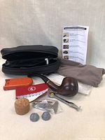 Photo showing all items included: wooden smoking pipe, black zippered case, cork stopper, red filter tips box, metal tools, cleaning cloths, and instruction sheet.