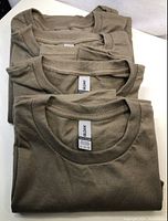 Five folded plain men's T-shirts in olive green color viewed from the neckline.