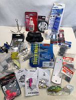 Various fishing tackle items including fishing weights, treble hooks, fishing line spool, lure bodies, glue, swivels, and plastic lure blade on a plain background