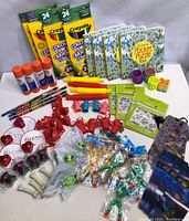 Full top-down view of all toys and art supplies for party loot bags on white surface, showing crayons, puzzle books, glue sticks, whistles, figurines, and games.