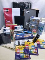 Wide view of assorted office supplies including notebooks, gloves, pens, staples, and sticky tabs.