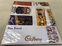 Photo showing the packaged tea towel with 'Tea Towel' and 'Cadbury' branding on the label.