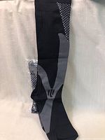 One black and grey knee-high compression sock laid out flat on a white surface with visible knit details and patterned designs.