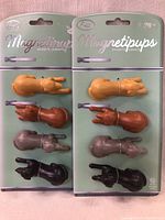 Front packaging photo showing four pairs of dog magnets in black, brown, gray, and tan arranged on mint green backing card labeled 'Fred Magnetipups'