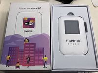 Box with Muama Ryoko portable wireless router visible inside, showing its compact size and digital display.