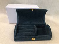Open black travel jewelry case showing padded ring rolls and a compartment inside, placed on a beige surface with a white outer box behind it.