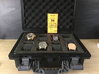 Four watches displayed in foam tray inside open black Invicta case