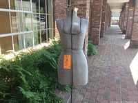 Front view of the Acme adjustable dress form with grey fabric cover, metal base, and visible adjustment seams.