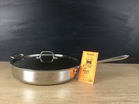 Full view of 13-inch All-clad stainless steel sauté pan with lid placed on a wooden surface, showing overall condition and shine.