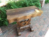 Image showing closed top of antique wooden card table with scalloped edges and carved base on brick patio.