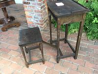 Full view of the antique telephone table and the folding seat from the side on a brick floor with a brick column background.