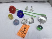 Full lot view showing 2 glass flowers (red and blue), 2 clear cat figurines with green eyes, 2 small paperweights (yellow and blue-pink), 2 crystal cube paperweights, a round magnifier paperweight, and a small spherical decorative piece.