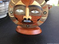 Close-up of hand-carved wooden circular mask with varying wood tones and inlaid eyes