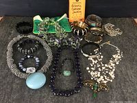 Full view of many costume jewelry pieces including necklaces, bracelets, brooch on a grey cloth background with a card reading 'Eclectic Costume Jewelry'.