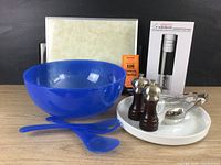 Overall lot view showing blue acrylic salad bowl with two matching servers, salt and pepper grinders on white ceramic tray with stainless tongs, electric corkscrew in box, vintage warming tray in background.