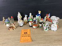 Full view of collection of diverse small ceramic figurines and miniatures from Occupied Japan arranged on wood surface, showing variety of characters and items