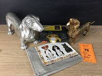 Overall lot showing both dachshund figures, Blue Q dog-themed tea towel, and Irish linen dog tea towel.