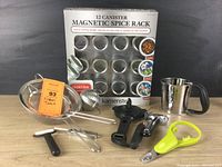 Photo showing the boxed 12-canister Kamenstein magnetic spice rack and various kitchen tools including strainers, jar opener, avocado tool, and peeler.