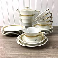 Full view of the set including stacked side plates, cups on saucers, and the teapot showing gold trim and design.