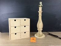 Wooden unfinished table lamp next to 6-drawer wooden storage box on table with black background